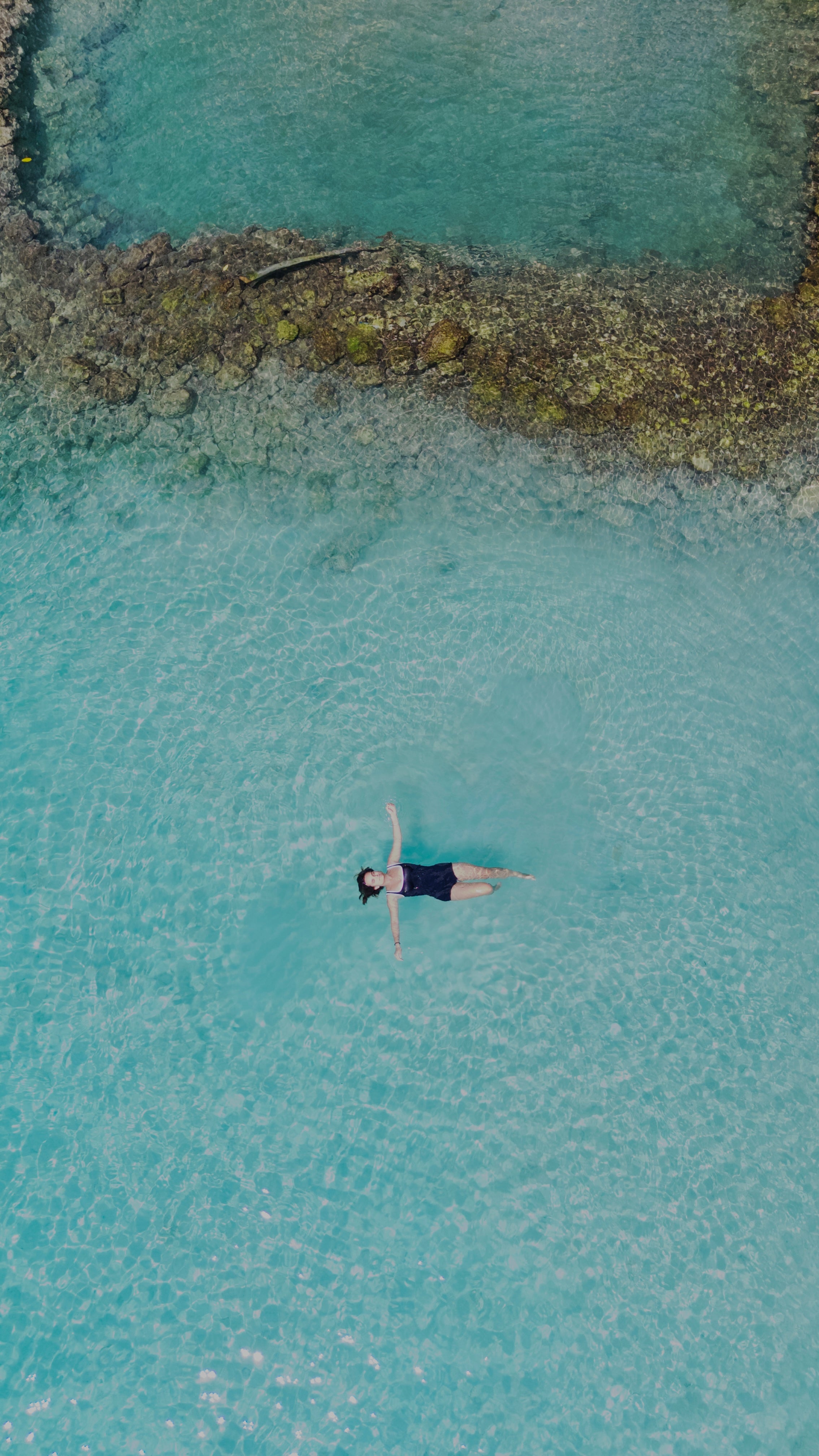 Person floating in clear blue water near a rocky shore